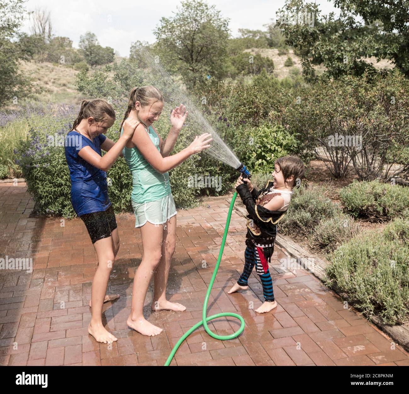 Kinder sprühen sich gegenseitig mit Wasserschlauch Stockfoto