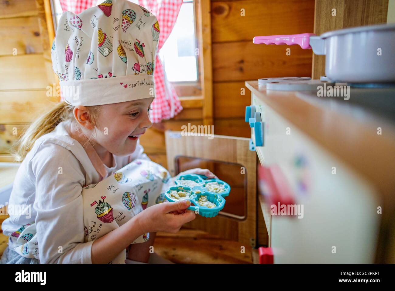 Junges Mädchen in wendy Haus Putting Tasse Kuchen im Ofen vorgibt, in der Küche zu kochen Stockfoto