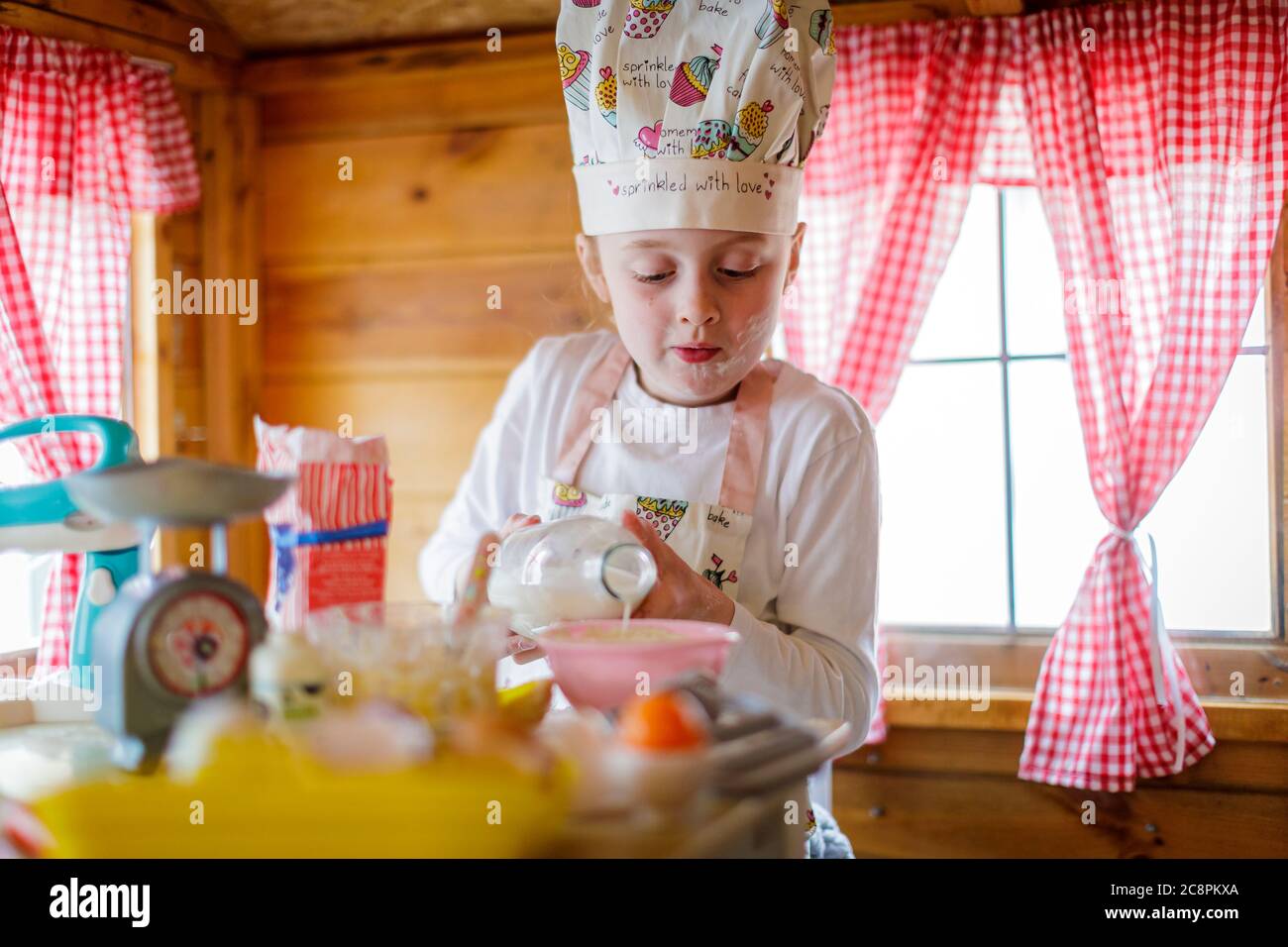 Junges Mädchen in wendy Haus Gießen Milch vorgibt, in der Küche zu kochen Stockfoto