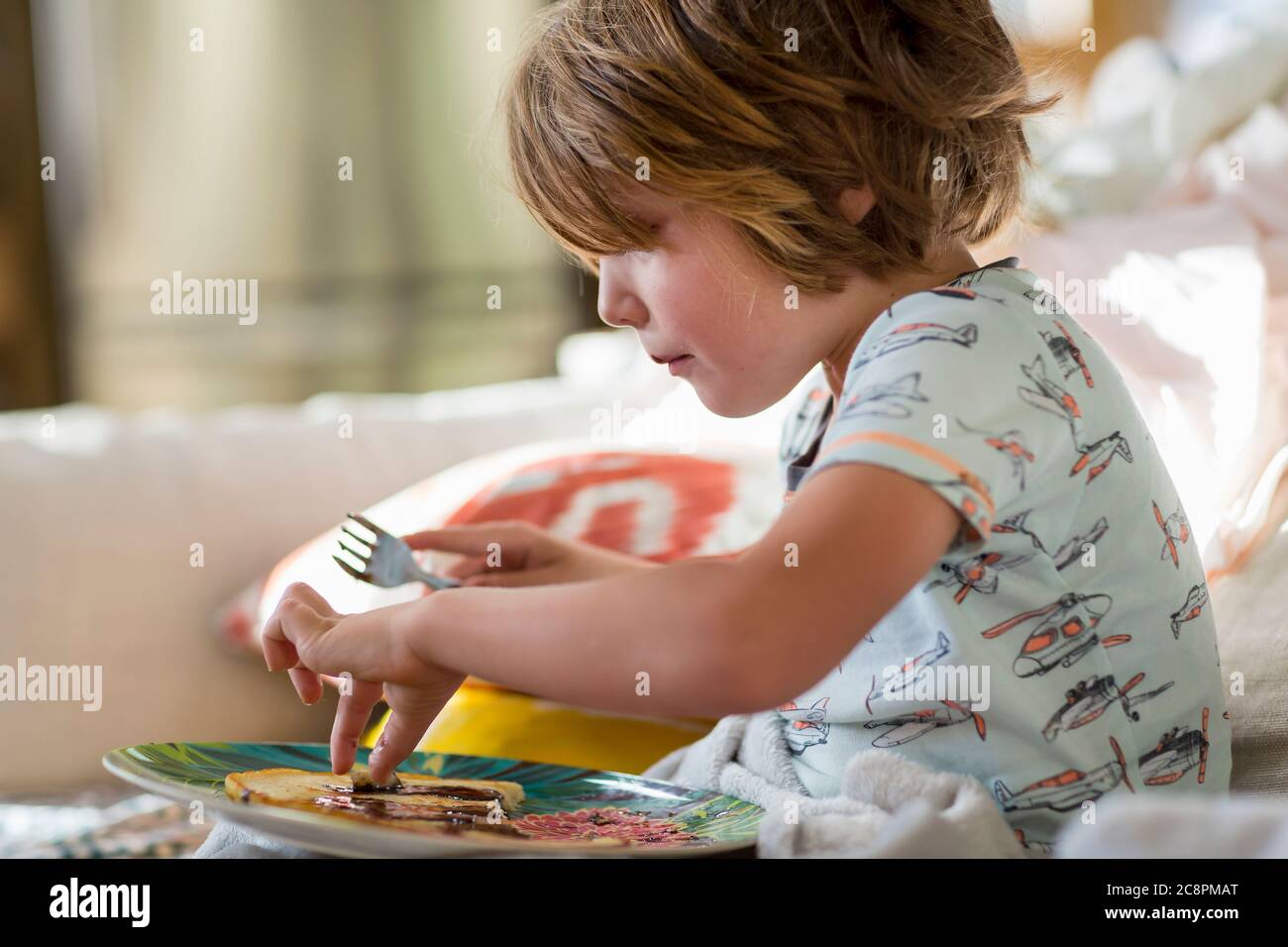 4 Jahre alter Junge, der Pfannkuchen auf dem Sofa isst Stockfoto
