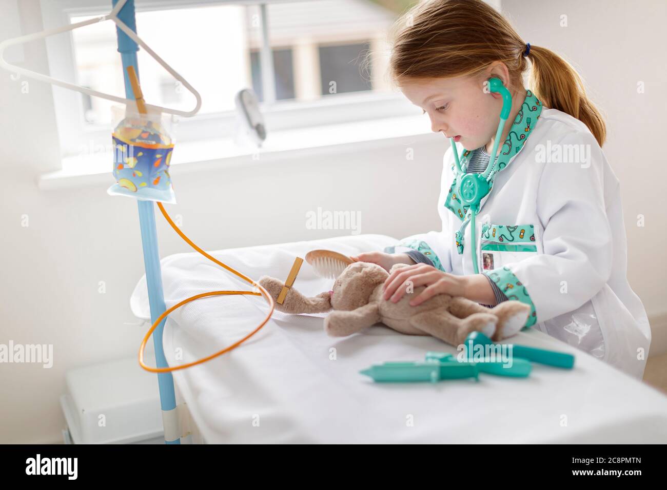 Junges Mädchen als Arzt gekleidet vorgibt, kuschelige Tier in Make-bleive Krankenhaus Bett zu behandeln Stockfoto