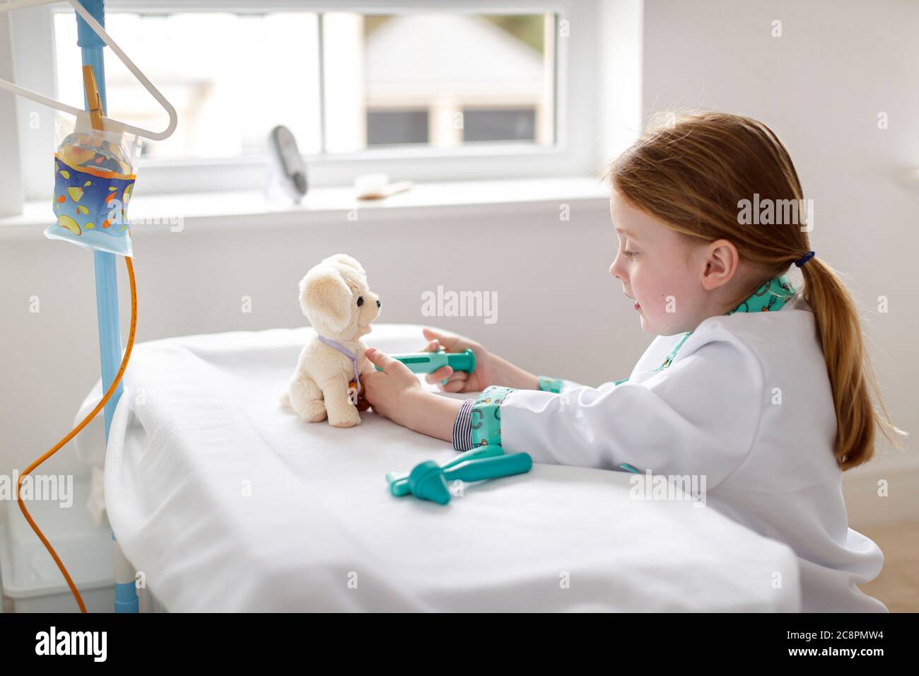 Junges Mädchen als Arzt gekleidet vorgibt, Spielzeug Hund in Make-bleive Krankenhaus Bett zu behandeln Stockfoto