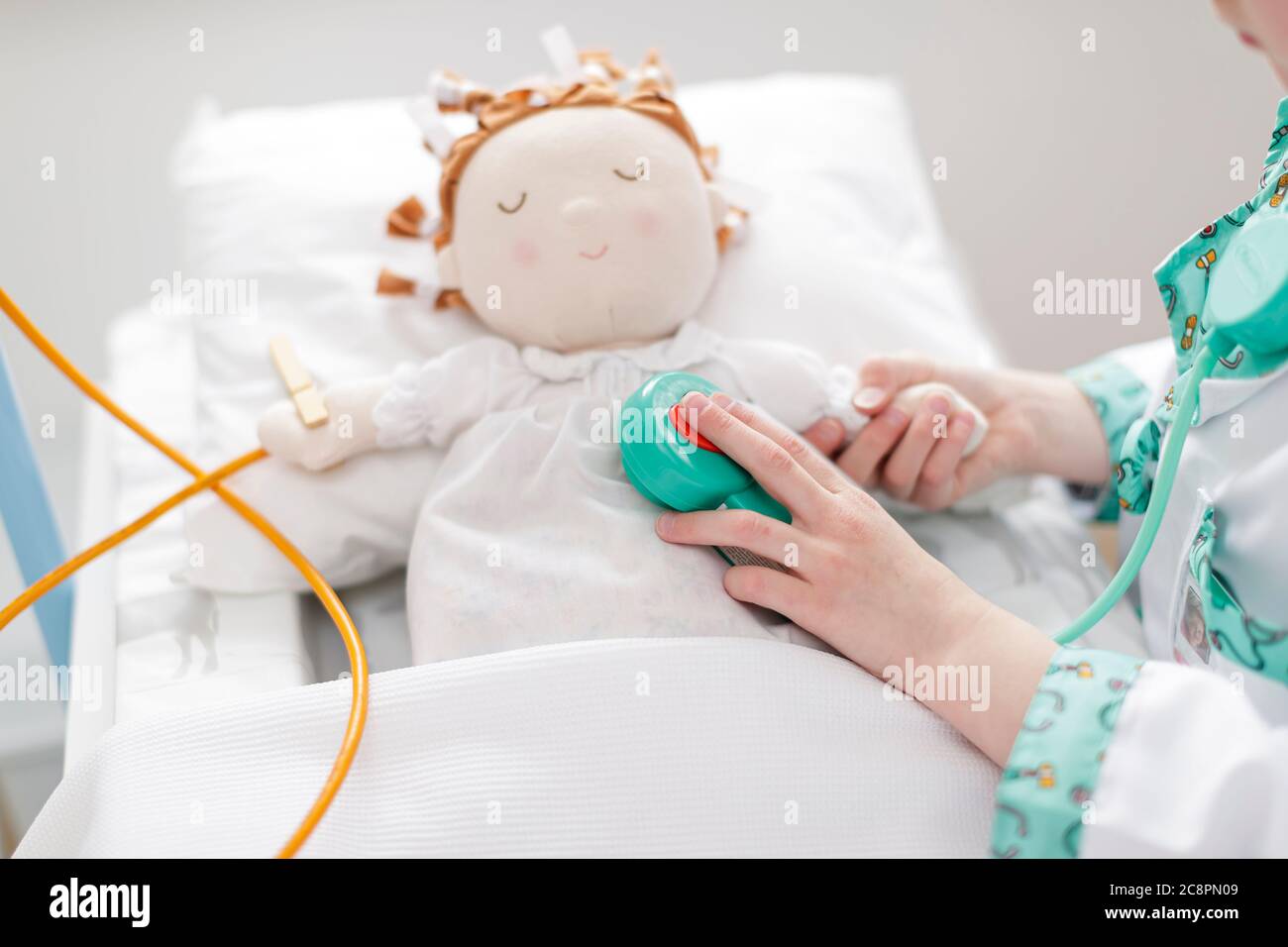 Junges Mädchen als Arzt mit Spielzeug Stethoskop auf Puppe in Make-glauben Krankenhaus Bett gekleidet Stockfoto