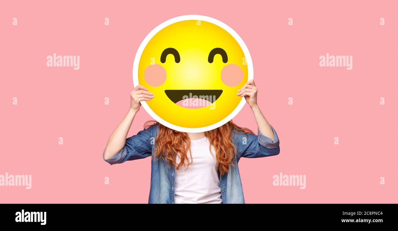 Rotschopf Mädchen versteckt ihr Gesicht hinter glücklichen emoji Lächeln Stockfoto