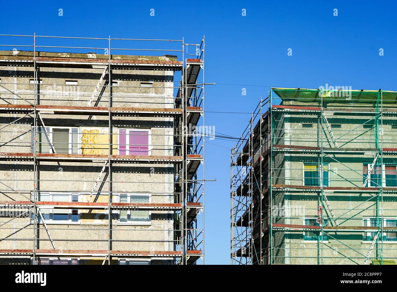 Gerüste, die eine Fassade eines Wohngebäudes bedecken, das in Renovierung auf einem blauen Himmel Hintergrund steht Stockfoto