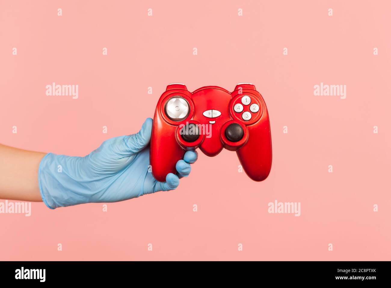 Profil Seitenansicht Nahaufnahme der menschlichen Hand in blauen OP-Handschuhe halten roten Gamepad Joystick. Indoor, Studio-Aufnahme, isoliert auf rosa Hintergrund. Stockfoto