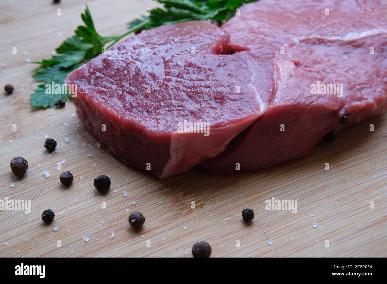 Rumpsteak. Stück 21 Tage gereiftes Rindfleisch auf dem Bambus-Holztisch mit schwarzem Pfeffer und Meersalzkristallen. Stockfoto