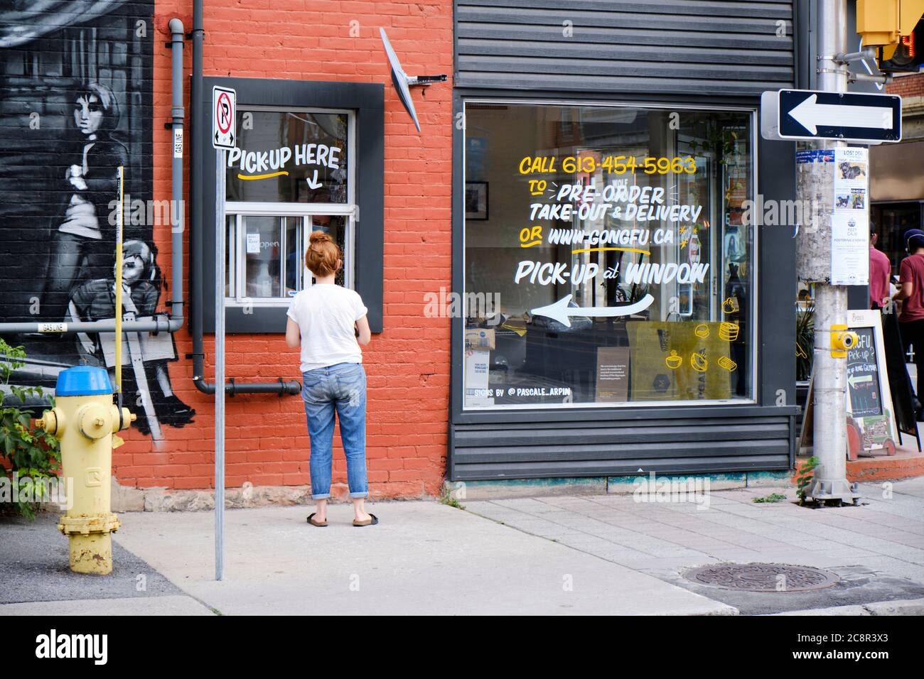 Junge Frau, die während der Pandemie 2020 Essen vom Fenster des Gong Fu Restaurants in Ottawa abholt Stockfoto