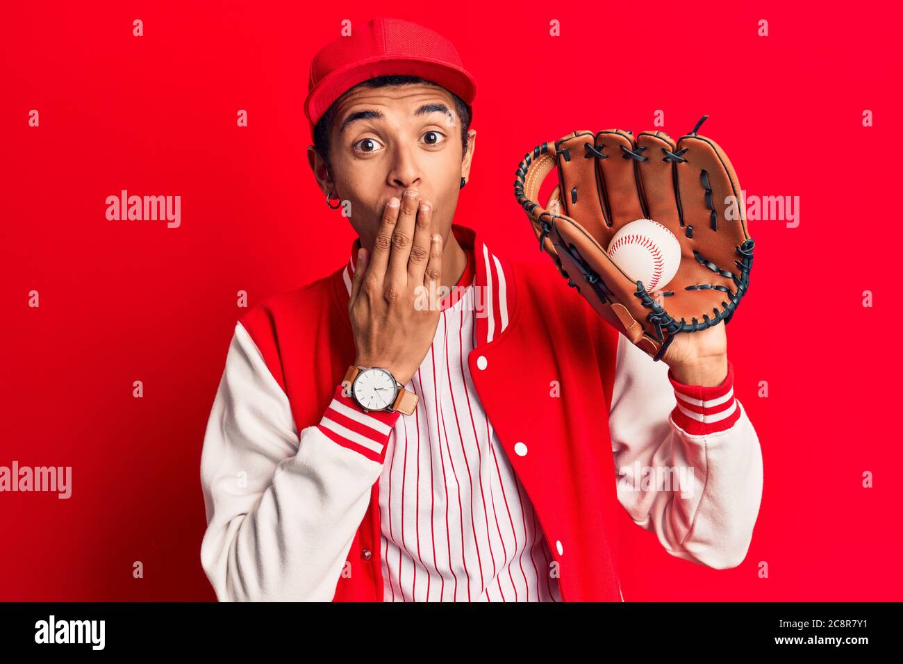 Junger afrikanischer amerikanischer Mann trägt Baseball Uniform hält Golve und Ball über den Mund mit der Hand, schockiert und Angst vor Fehler. Überrascht zum Ausdruck bringen Stockfoto