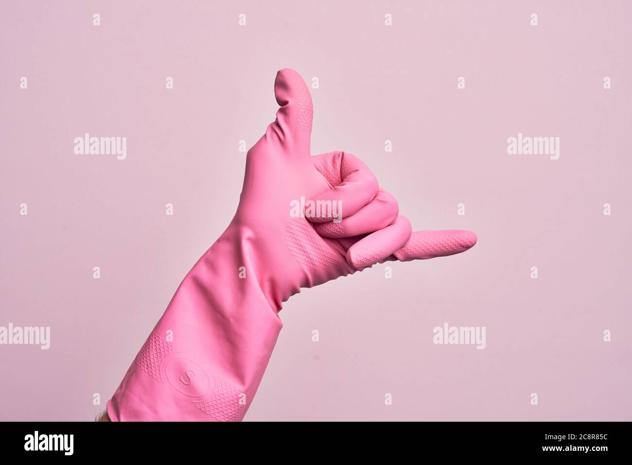 Hand des kaukasischen jungen Mannes mit Reinigungshandschuh über isolierten rosa Hintergrund gestikulierenden Hawaiian shaka Grußgesten, Telefon und Kommunikation s Stockfoto