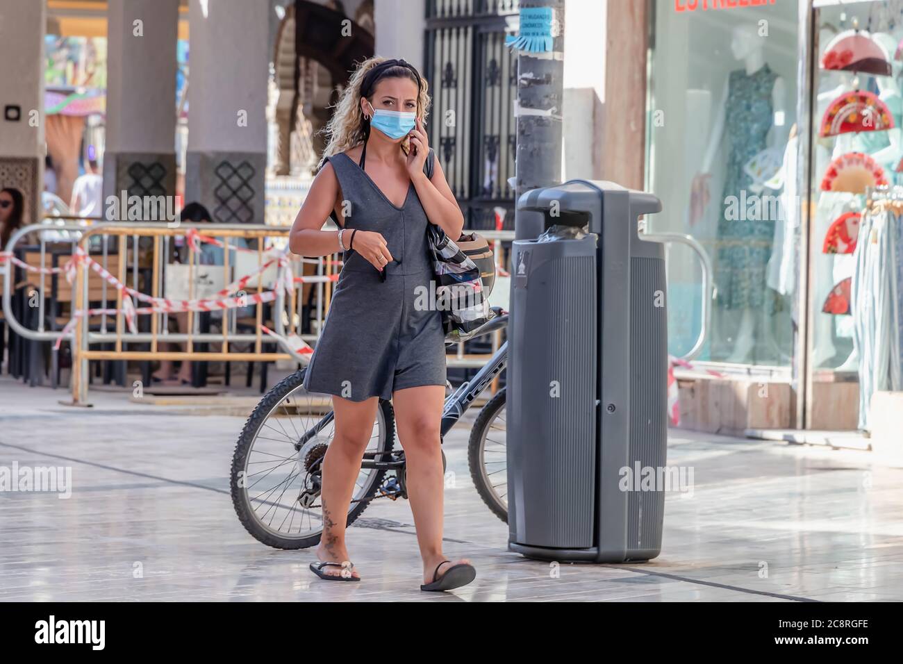 Punta Umbria, Huelva, Spanien - 10. Juli 2020: Frau mit ihrem Handy geht mit Schutzmaske auf der Straße wegen covid-19. Neue normale in Stockfoto