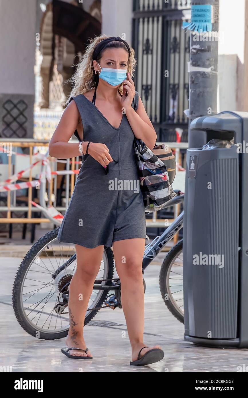 Punta Umbria, Huelva, Spanien - 10. Juli 2020: Frau mit ihrem Handy geht mit Schutzmaske auf der Straße wegen covid-19. Neue normale in Stockfoto