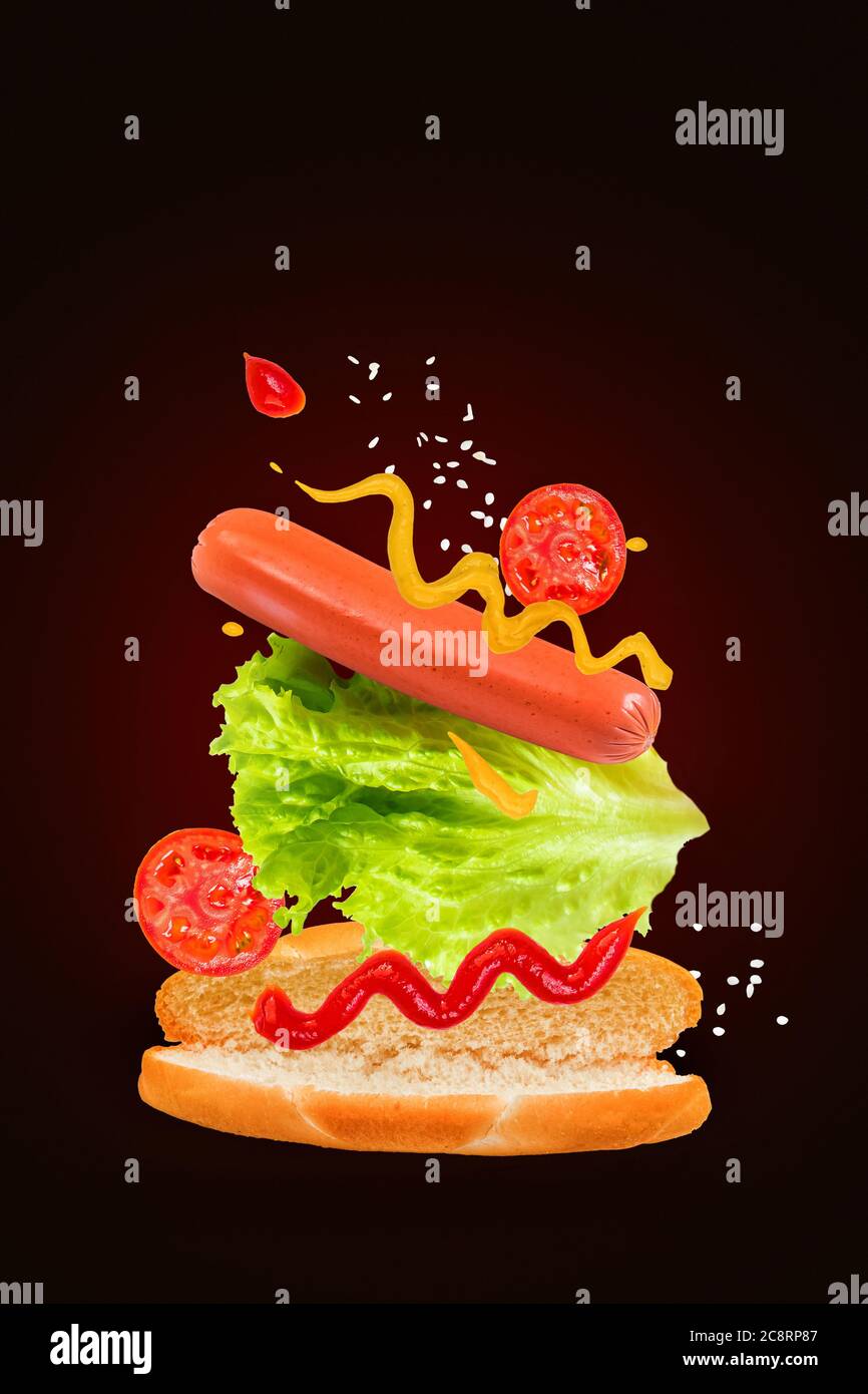 Köstlicher Hot Dog mit fliegenden Zutaten auf dunklem Hintergrund. Schwebendes Essen. Stockfoto