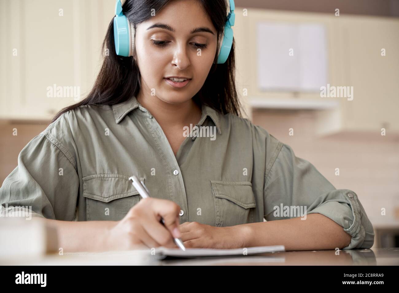 Indische Mädchen tragen Kopfhörer schreiben Hausaufgaben hören Audio-Kurs zu Hause. Stockfoto