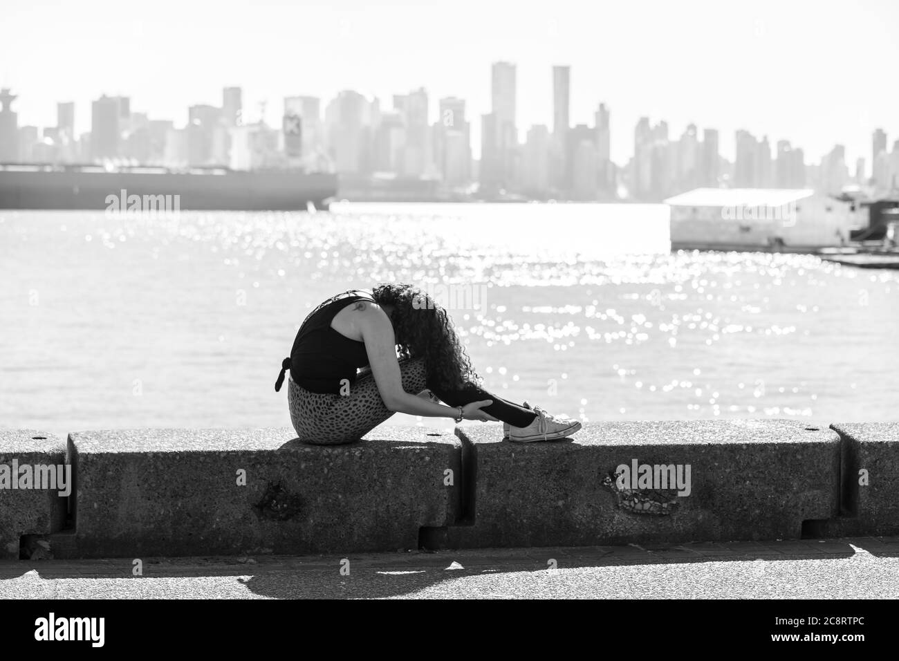 Junge Frau, die Yoga auf der Ufermauer mit Vancouver City im Hintergrund macht Stockfoto