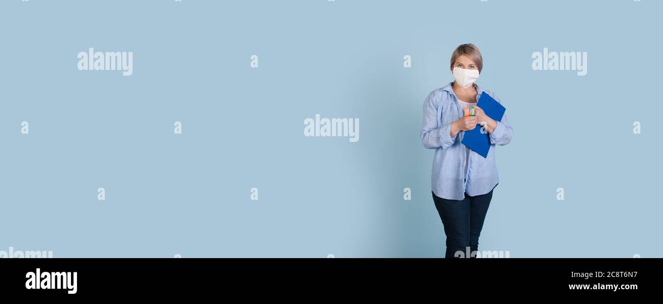 Ältere kaukasische Geschäftsfrau mit medizinischer Maske auf Gesicht hält einen Ordner und Marker posiert auf einer blauen Studio-Wand mit freiem Platz Stockfoto