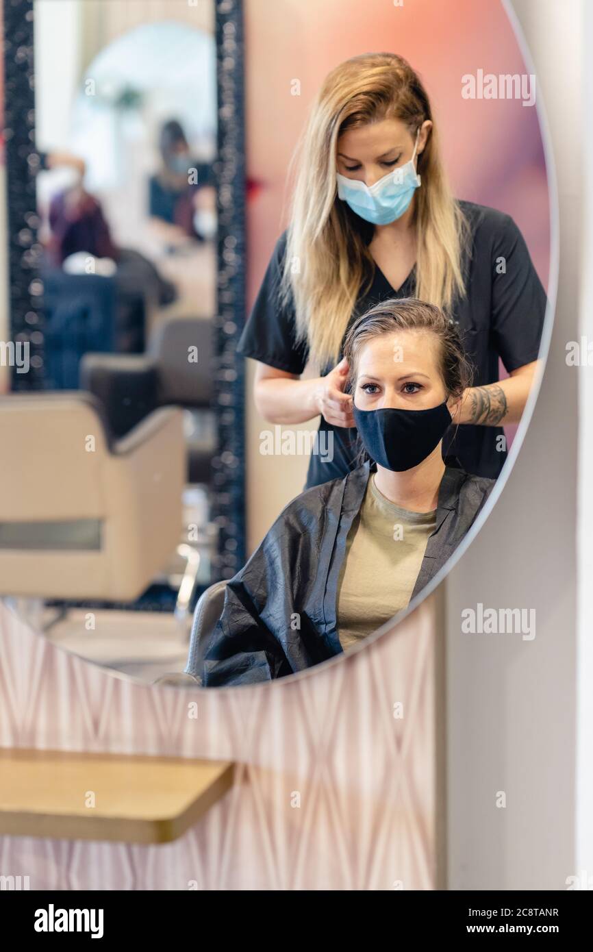 Friseur Trocknen der Haare ihrer Kunden mit einem Haartrockner tragen Schutzmasken in einem Beauty-Center. Stockfoto