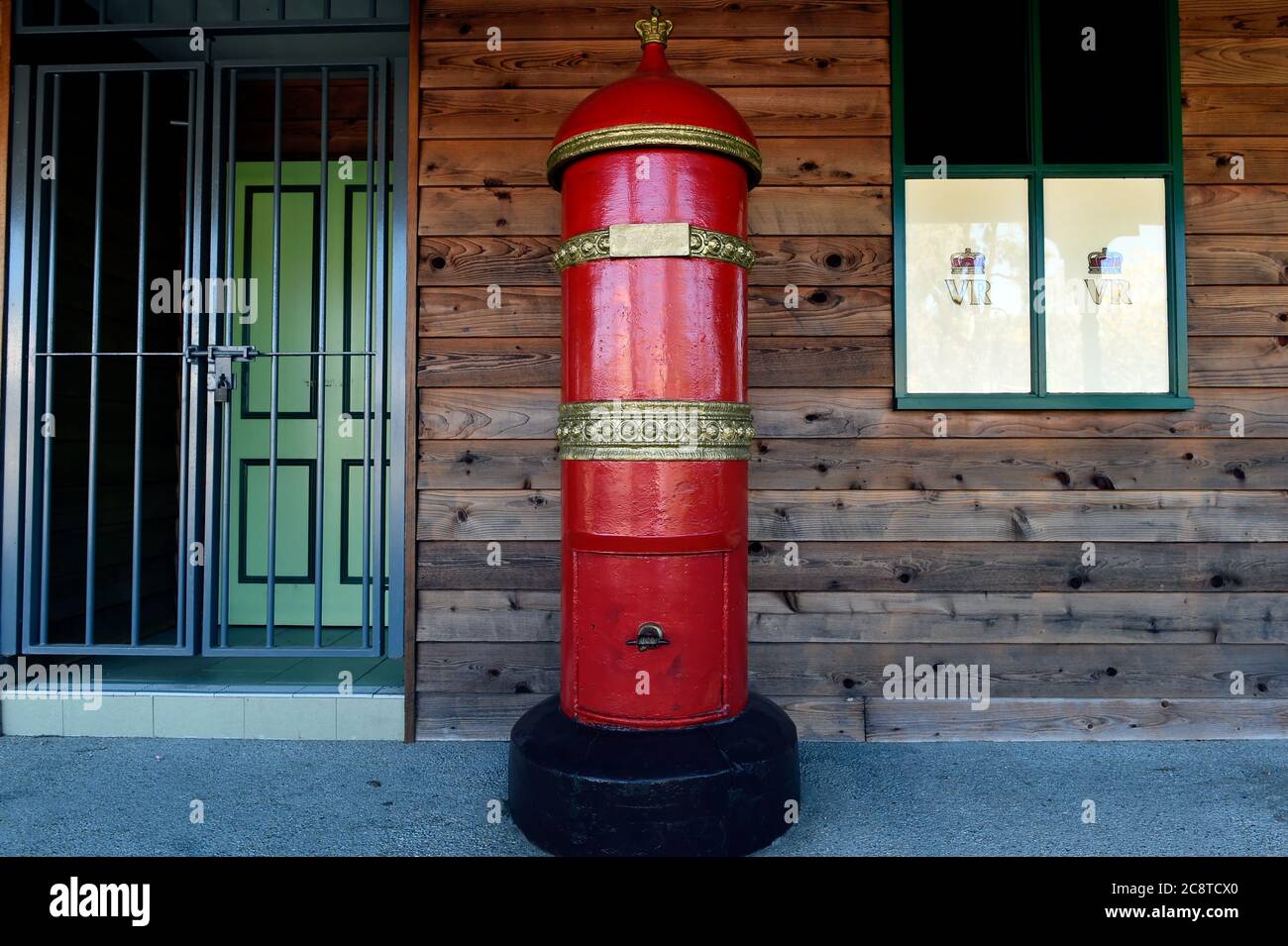 Glenrower, Victoria. Ein leuchtend roter alter australischer Briefkasten steht hoch vor einem mit Holz verkleideten Gebäude in der historischen Stadt Glenrowan in Victoria's Stockfoto