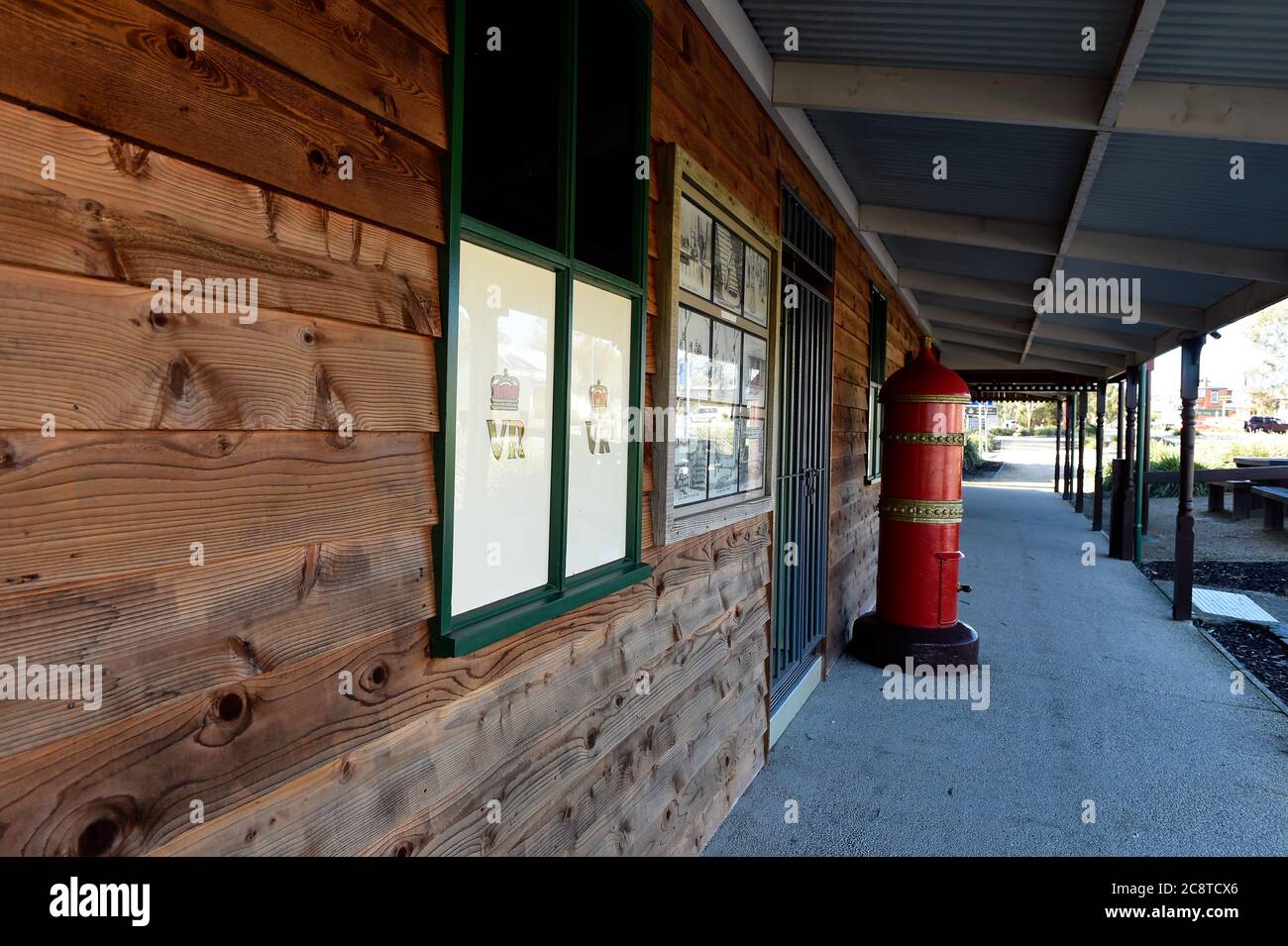 Glenrower, Victoria. Ein leuchtend roter alter australischer Briefkasten steht hoch vor einem mit Holz verkleideten Gebäude in der historischen Stadt Glenrowan in Victoria's Stockfoto