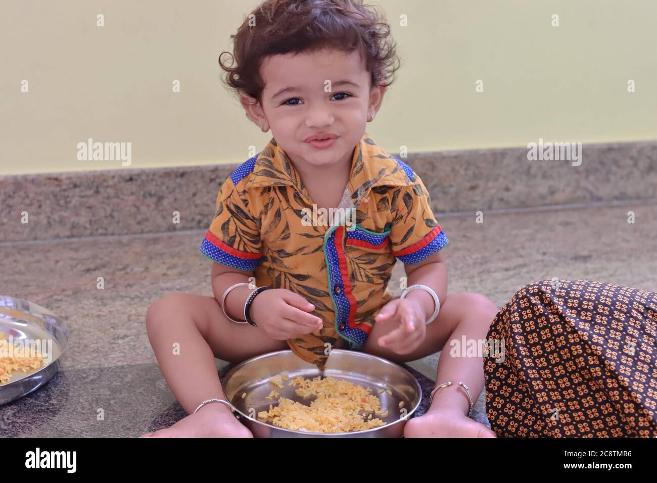 Ein Kind sitzt im Haus und isst Essen und der kleine Junge hat einen Teller voll mit Essen Stockfoto