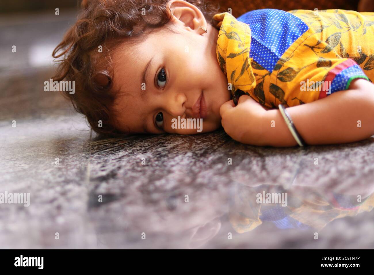 Ein Kind, das auf dem schwarzen Marmorboden auf die Kamera schaut Stockfoto