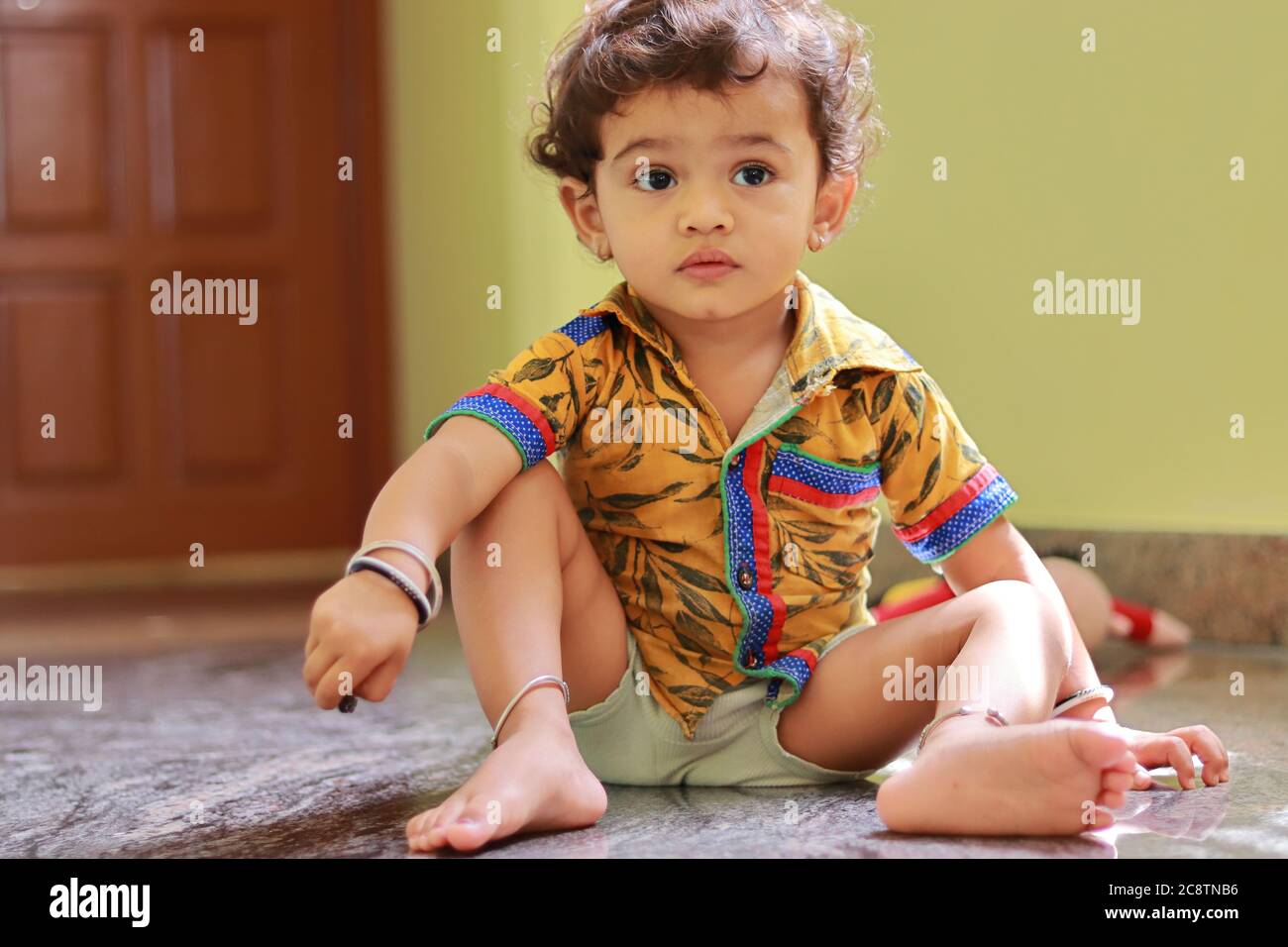 Ein Kind sitzt auf dem Boden im Haus und ein kleiner Junge mit einer Hand auf dem Knie Stockfoto
