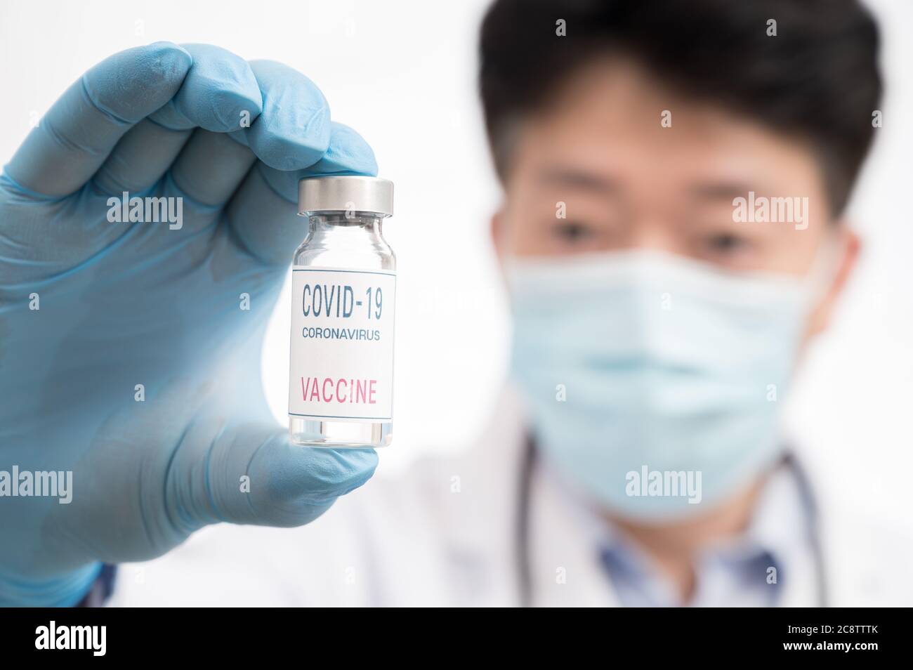 Die Hand des Arztes trägt blaue Handschuhe vor weißem Hintergrund und hält den Covid-19-Impfstoff. Stockfoto