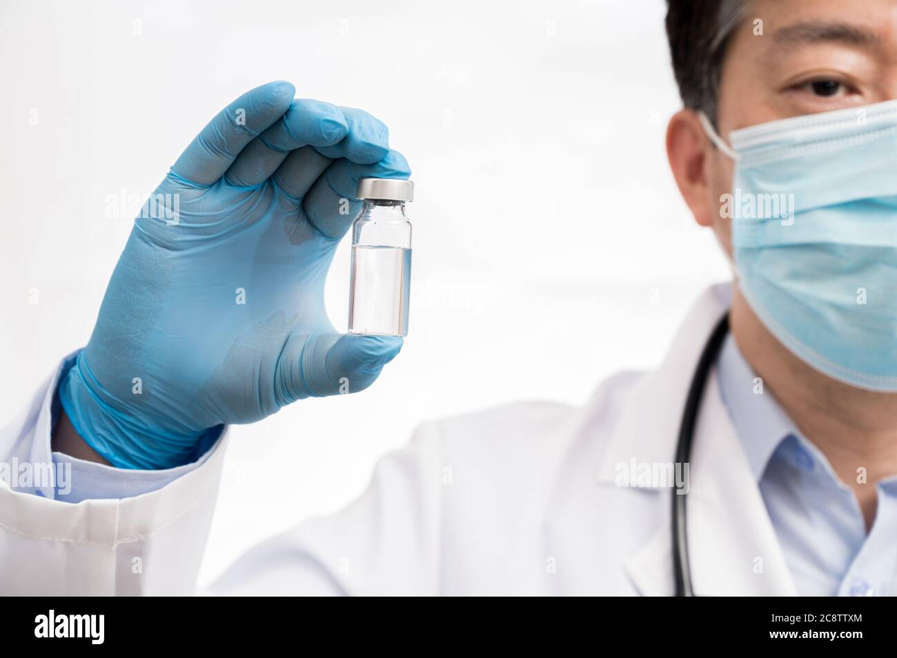 Die Hand des Arztes trägt blaue Handschuhe vor weißem Hintergrund und hält den Covid-19-Impfstoff. Stockfoto