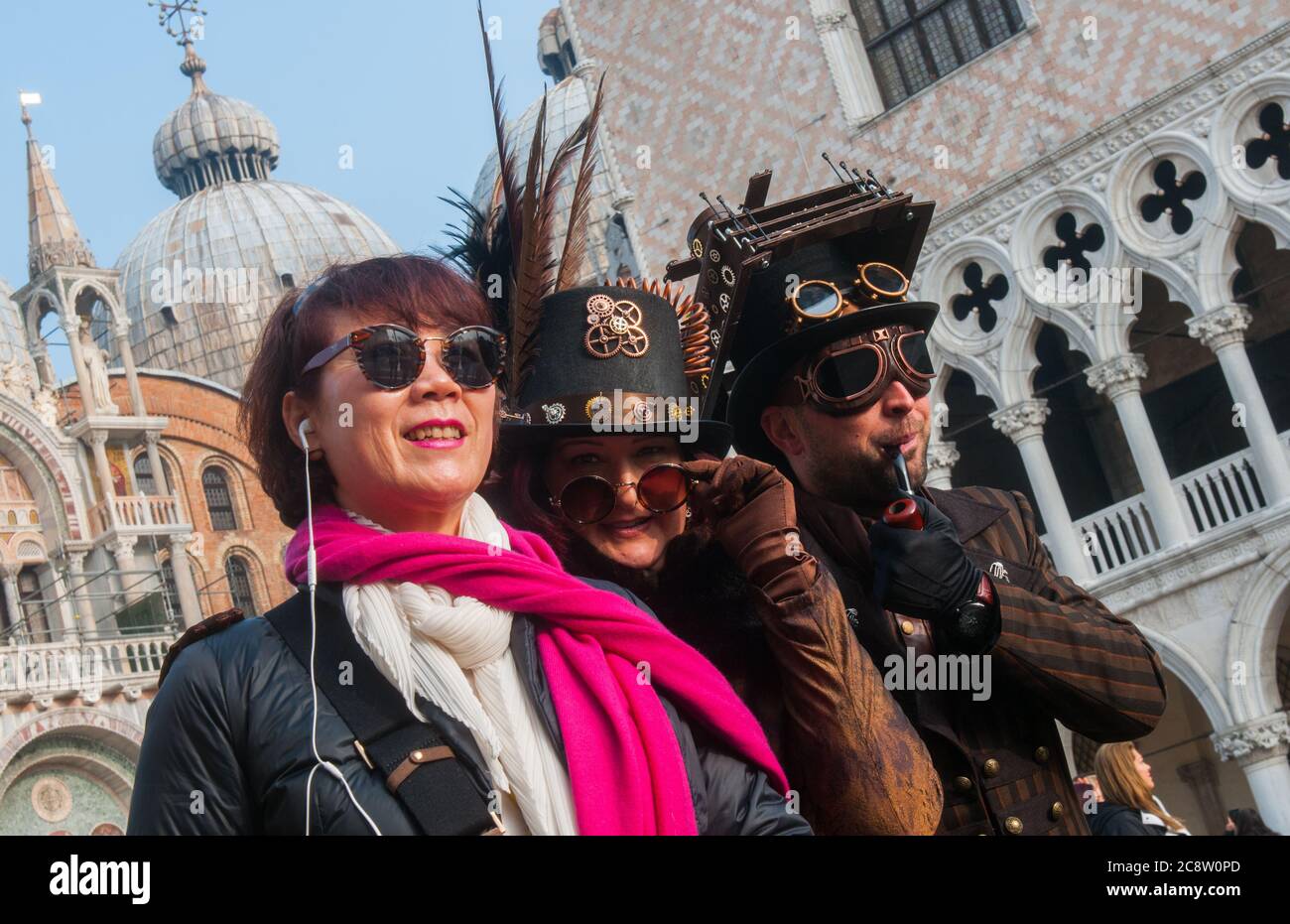VENEDIG, ITALIEN - 28. FEBRUAR 2020: Zwei Steampunk Masken posieren mit einem Touristen während des Karnevals in Venedig Stockfoto