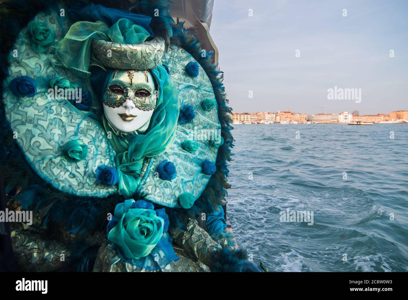 Eine wunderschöne Maske posiert vor dem Venedig Kanal in einem hellblauen Kostüm mit Rose. Stockfoto