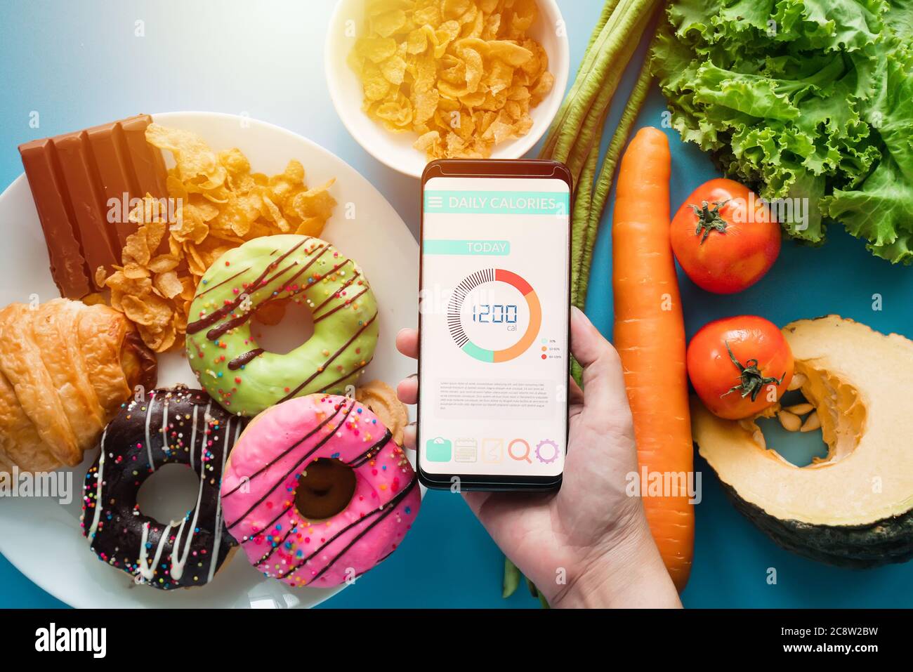 Kalorienzählen und Lebensmittelkontrolle Konzept. Frau mit Kalorienzähler Anwendung auf ihrem Smartphone mit frischem Gemüse, Dessert und Donuts Stockfoto