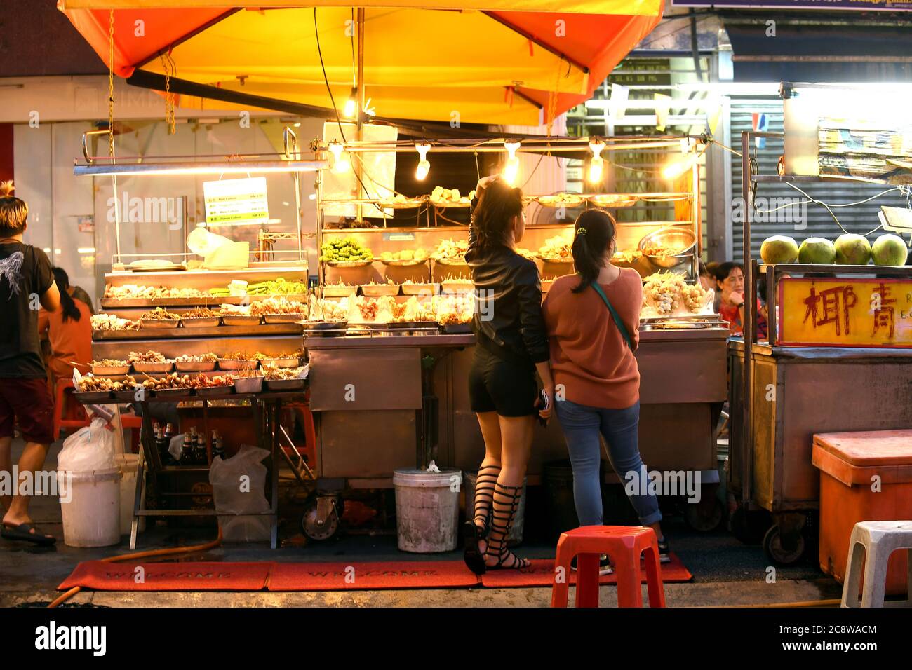 Zwei junge Frauen wählen an einem Street-Food-Stand in Kuala Lumpurs Chinatown aus frischem Essen. Stockfoto