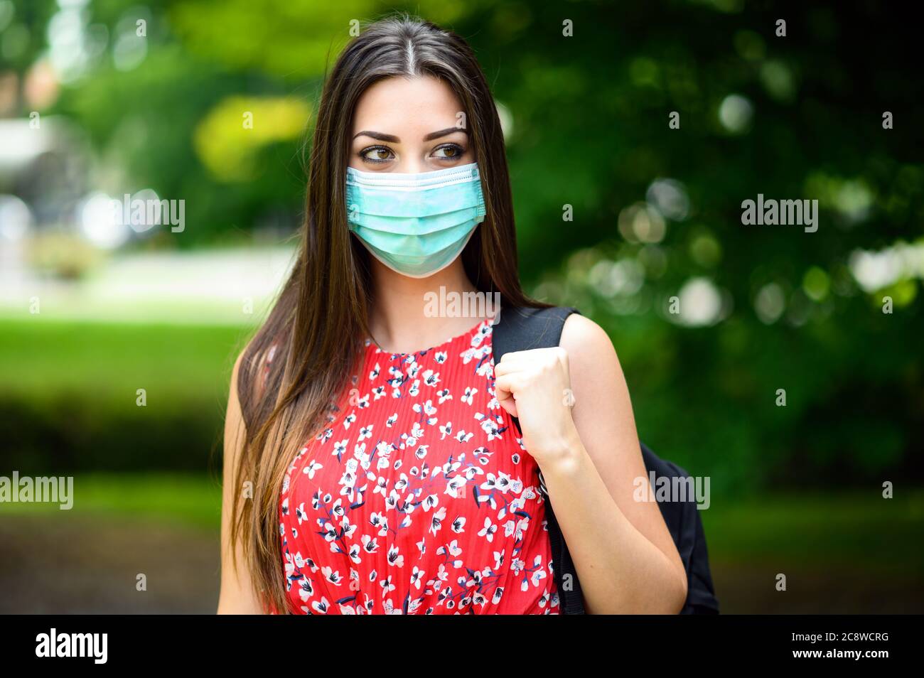 Studentin, die im Park spazieren geht und eine Maske trägt, um sich vor dem Coronavirus zu schützen Stockfoto