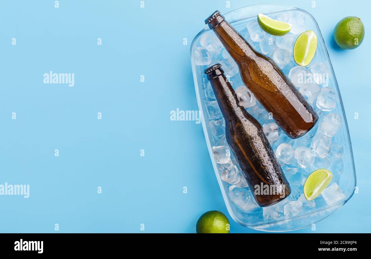 Sommer mit Getränk. Zwei Glasflaschen in Glastablett mit Eis und Limette auf blauem Hintergrund Stockfoto