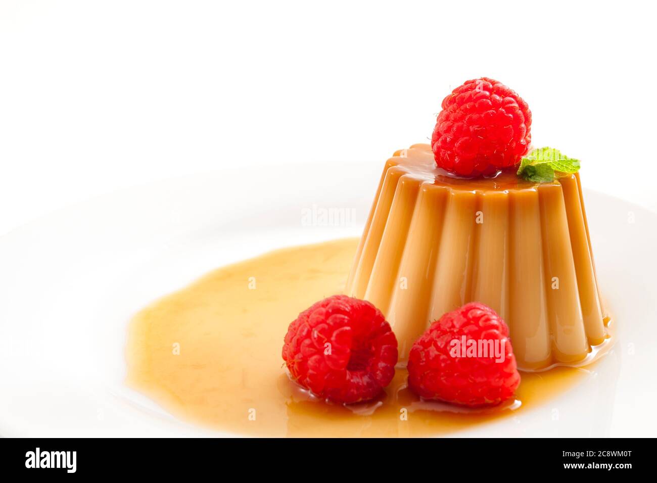 Hausgemachtes Dessert und glatte Pudding Süßigkeiten Konzept mit Nahaufnahme auf Creme Karamell, Flan oder Karamell Pudding mit süßen Sirup und Himbeeren iso bedeckt Stockfoto