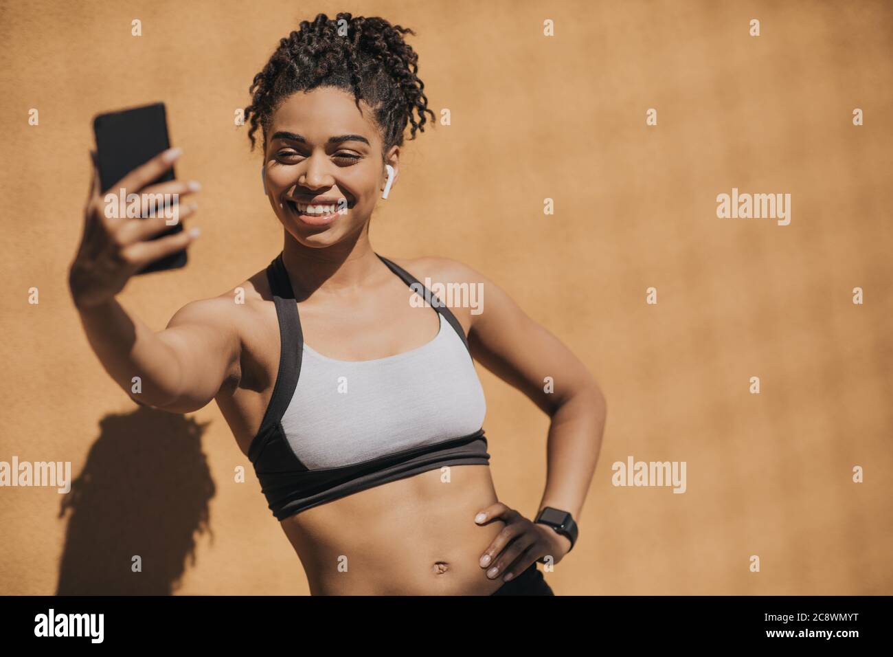 afroamerikanische junge Frau in Sport-BH mit kabellosen Kopfhörern und  Fitness-Tracker macht Selfie Stockfotografie - Alamy