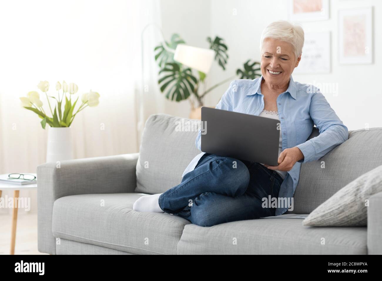 Entspannen Sie Sich Zu Hause. Positive Ältere Frau Ruht Mit Laptop Auf Der Couch, Filme Ansehen Stockfoto