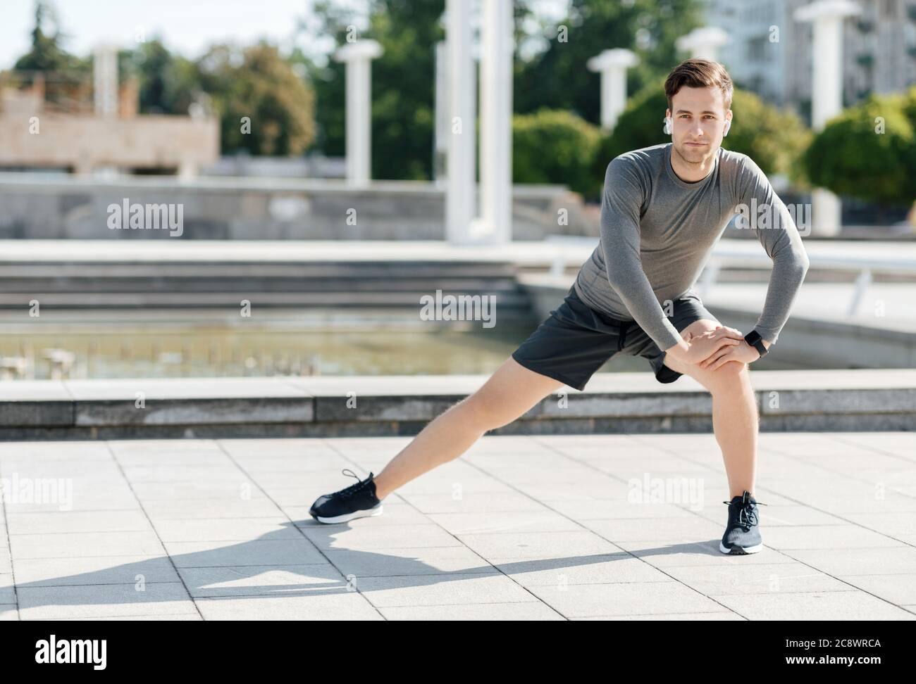 Training vor dem Marathon. Mann mit kabellosen Kopfhörern macht Übungen für Beine Stockfoto