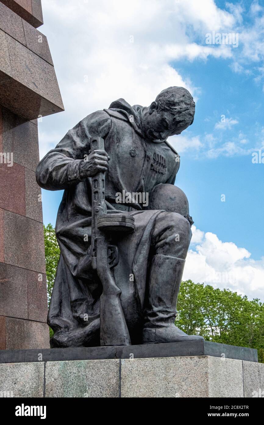 Bronzeskulptur eines knienden Soldaten, der Waffe und Helm vor einer abstrakten Granitfahne am sowjetischen Kriegsdenkmal im Treptow Park, Berlin, hält Stockfoto
