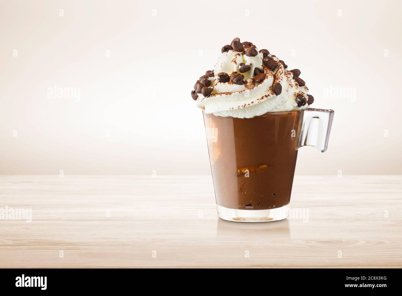 Tasse Kaffee mit Schlagsahne, Kakaopulver und Schokoladenstückchen auf Holztisch. Stockfoto