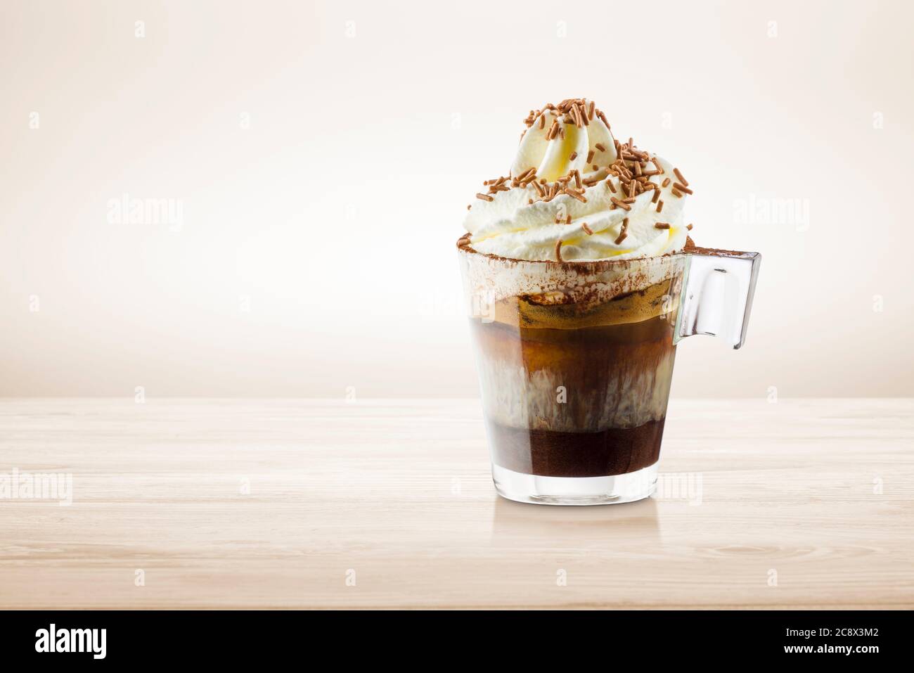 Tasse Kaffee mit Schlagsahne, Milchschaum und Schokoladenstückchen auf Holztisch. Stockfoto