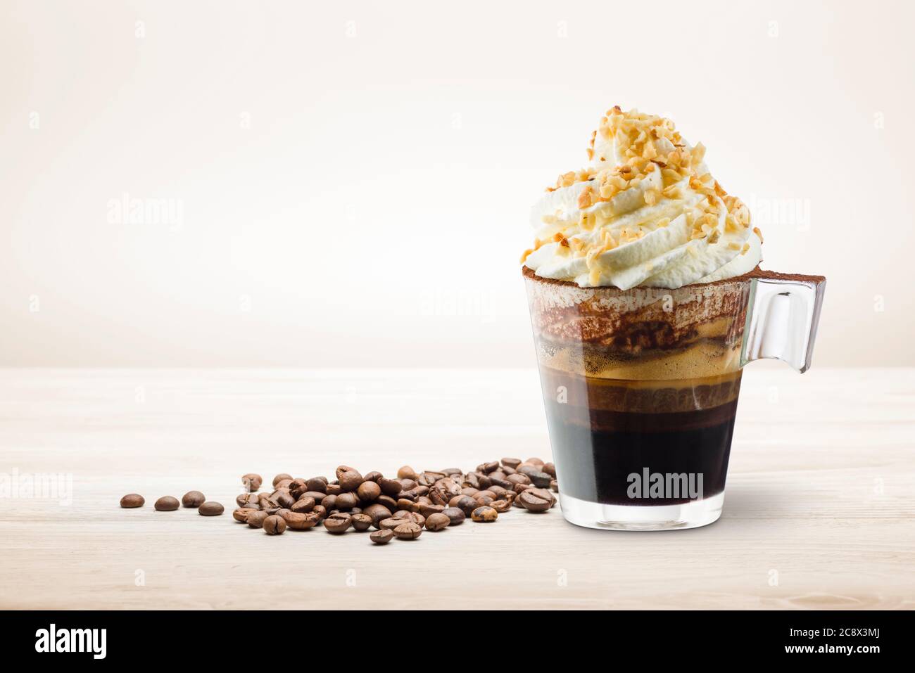 Tasse Kaffee mit Schlagsahne, Schokoladenschaum und Haselnusskorn auf Holztisch. Stockfoto