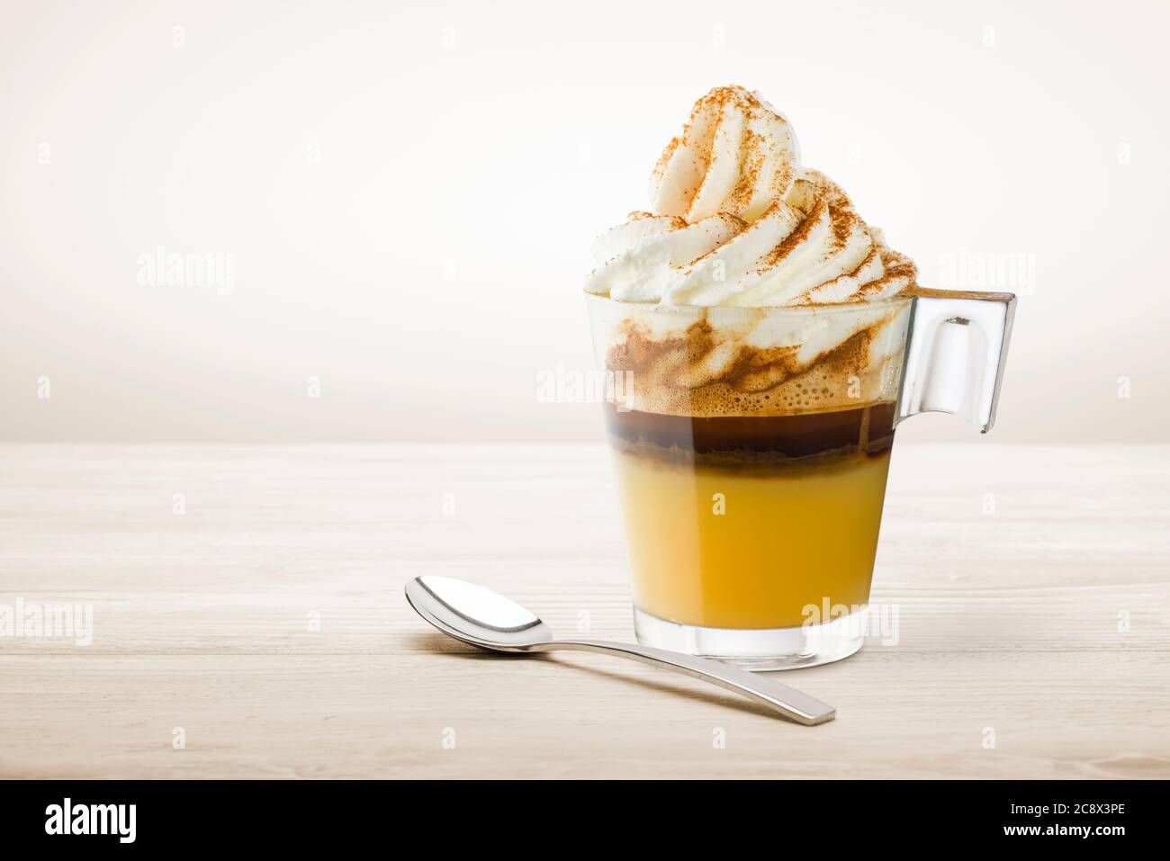 Tasse Kaffee mit Schlagsahne, Karamellcreme und Zimtpulver auf Holztisch. Stockfoto