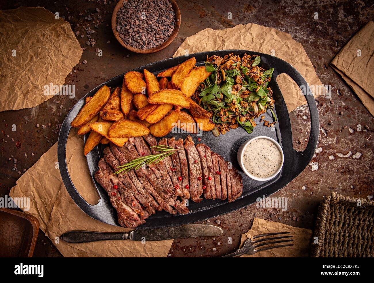 Rindersteak und Kartoffeln mit Pfeffersauce und Salat auf schwarzem Teller, Draufsicht Stockfoto
