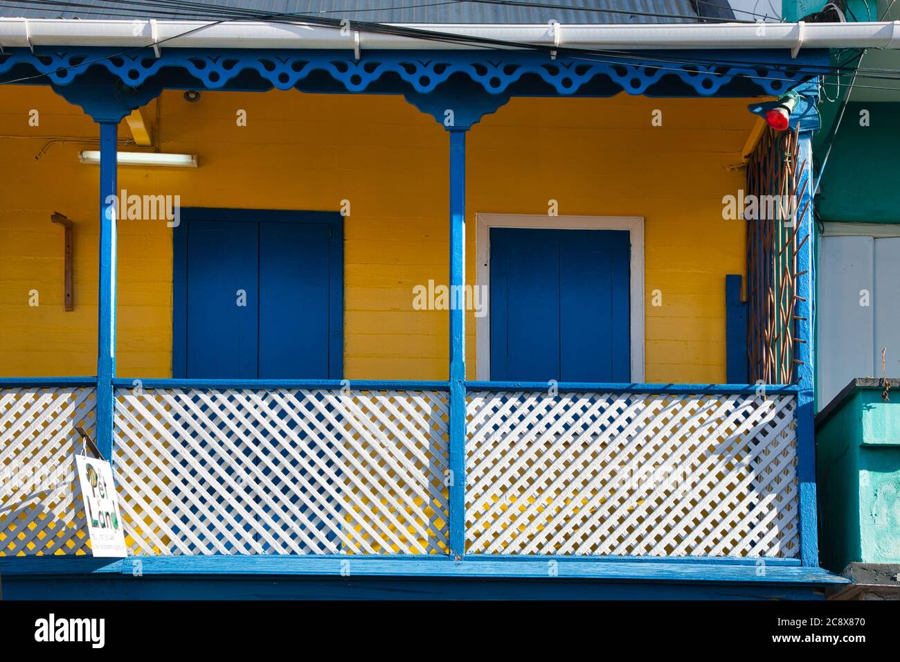 Hübsche bunte Veranda auf einem Haus mit blau-weißen Geländern und gelben Wänden in Roseau, Dominica Insel, der Karibik Stockfoto