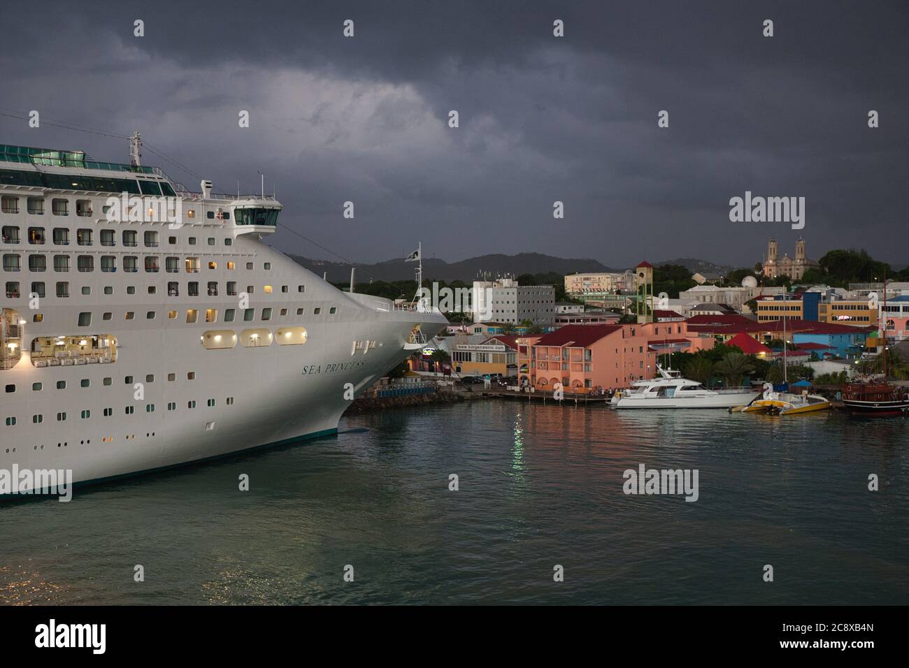 Das Bug eines Kreuzfahrtschiffes im Hafen von St Johns, Antigua, Karibik, mit dunklen Sturmwolken über der Dämmerung Stockfoto