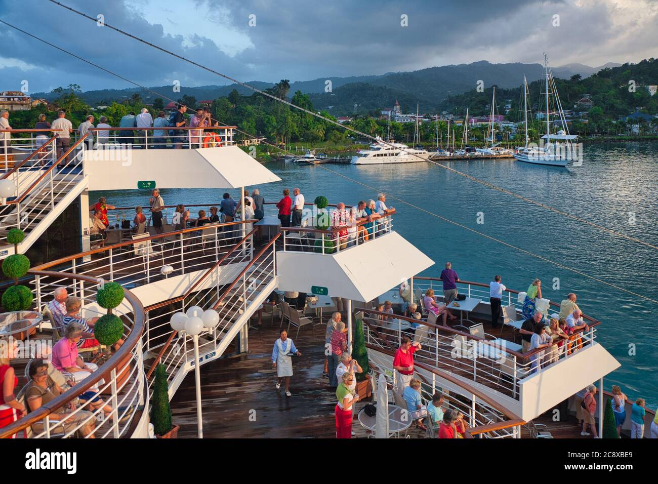 Die Leute am Geländer eines Kreuzfahrtschiffes beobachten, wie das Schiff mit anderen bereits festfahrenden Booten in Jamaika, der Karibik, in den Hafen kommt Stockfoto