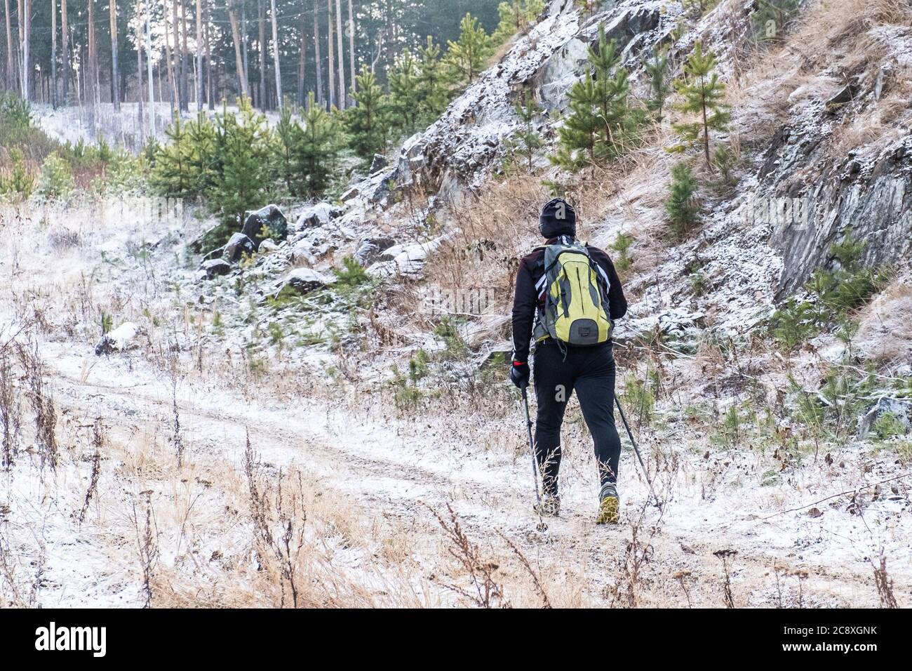 Jekaterinburg, Russland - 9. November 2019: Ein Mann mit Rucksack mit skandinavischen Wanderstöcken im schwarzen Sportanzug und Sneakers geht durch den Berg Stockfoto