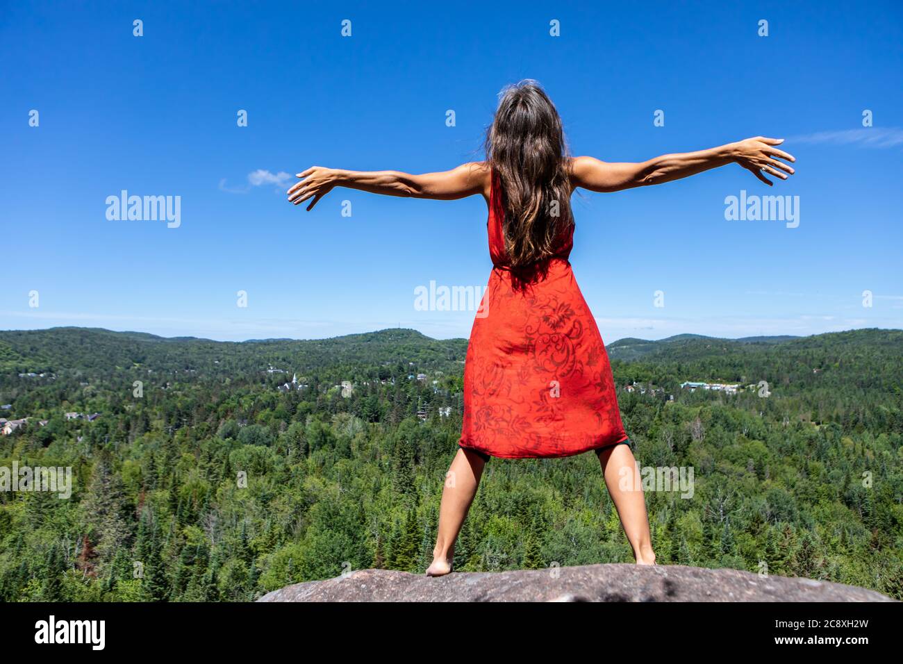 Blick von hinten auf eine junge Frau in einem roten Kleid, die ihre Arme weit öffnet und ihren Kopf in den Himmel hebt, vor einer kanadischen Berglandschaft. Stockfoto