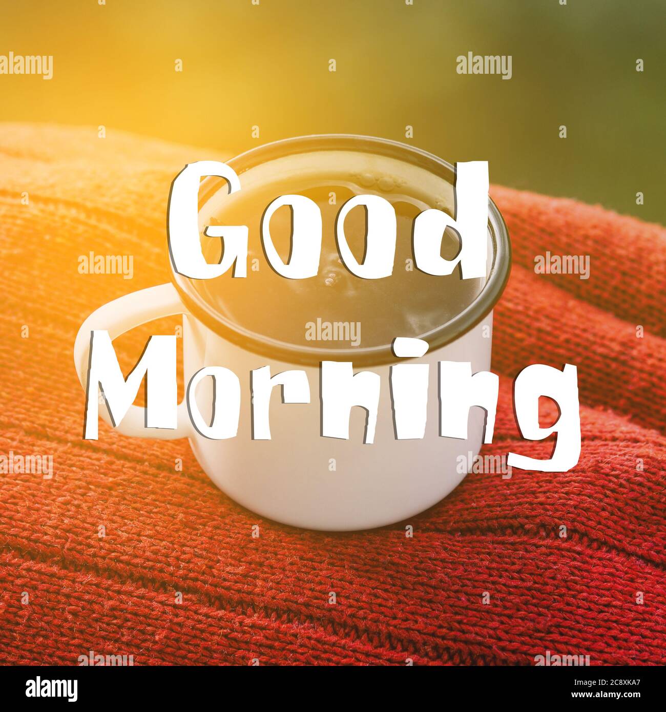 Kaffeetasse und ein Schild mit dem Text Guten Morgen. Metallbecher auf einem roten Pullover. Stockfoto